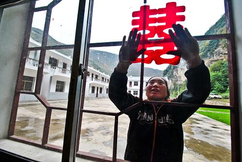 在贵州省威宁县云贵乡水塘村河边组,一名村民在灾民安置点帮助准备结婚的邻居粘贴“喜”字窗花(2013年12月8日摄)。新华社发(杨文斌 摄)